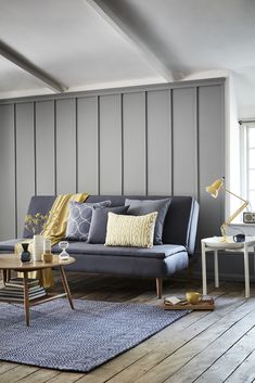 a living room with gray walls and wooden floors, blue couches and yellow throw pillows