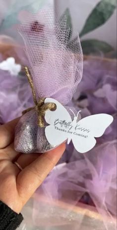 a hand holding a small white butterfly ornament on top of purple tulle