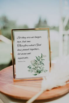 a sign that is on top of a wooden table next to a white feather and some flowers