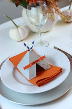 a white plate topped with an origami tent next to a vase filled with flowers