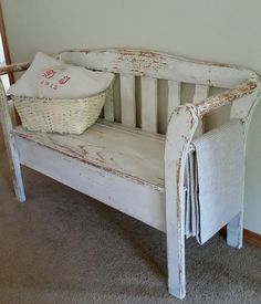 an old white bench with a basket on the back and some pillows sitting on top of it