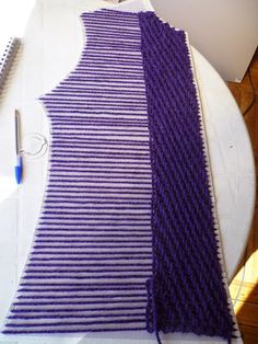 a piece of purple yarn sitting on top of a white table next to a pen