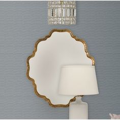 a white table lamp sitting next to a wall mounted mirror on the side of a gray wall