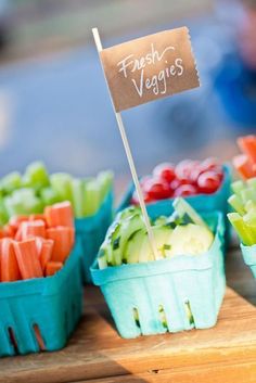 fresh veggies are displayed in plastic baskets on a wooden table with a sign that says fresh veggies