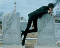 a man in a suit leaning on the headstones of graves