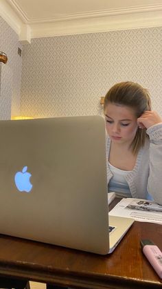 a woman sitting in front of a laptop computer on a wooden desk next to a lamp