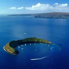 an island in the middle of the ocean with boats floating on it's surface