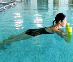 a woman is swimming in the pool with yellow cylinders