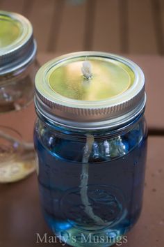 two mason jars with lids are sitting on a table next to each other and one has a candle in it