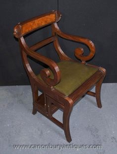 an old chair with a green seat and wooden arm rests against a black wall behind it