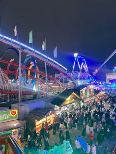 an amusement park at night with people walking around and rides on roller coasters in the background