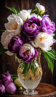 a vase filled with lots of purple and white flowers on top of a wooden table