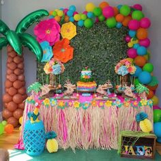 a table topped with lots of colorful balloons and desserts next to a wall covered in pom - poms