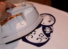 a person using an iron on top of a white table cloth with a cartoon design