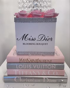 three books stacked on top of each other in front of a flower vase with pink roses