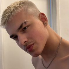 a man with blonde hair and piercings on his forehead looking at the camera in front of a mirror