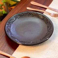 a black plate sitting on top of a wooden table next to utensils and spoons