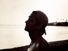 a black and white photo of a man in front of the water looking up at something