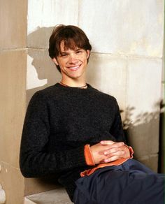 a young man sitting on the ground smiling