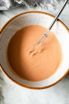 a bowl filled with sauce and whisk on top of a marble countertop