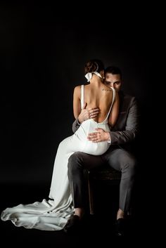 a man and woman sitting on top of a chair in front of a black background