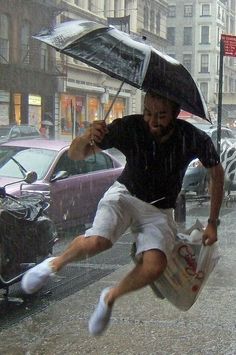 a man jumping in the air while holding an umbrella over his head on a rainy day