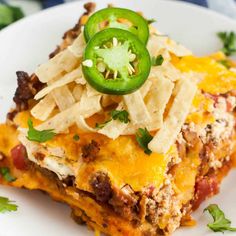 a slice of mexican lasagna on a plate topped with cheese and jalapenos