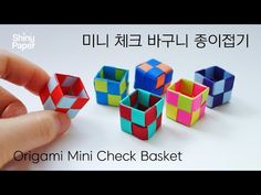 a hand holding an origami check basket in front of several small cubes