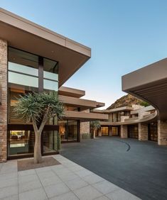 an empty parking lot in front of a large building with many windows and plants on it