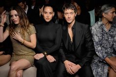 three people are sitting next to each other in front of a group of others at a fashion show