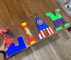 a person holding scissors next to cut out letters on a wooden table with other items