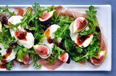 figs and prosciutto salad on a white platter with blue background