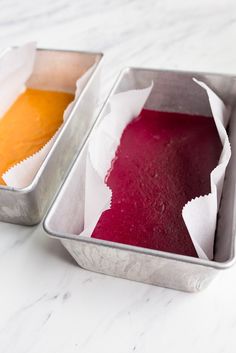 two tins filled with red and yellow food on top of a white marble counter