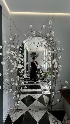 a man standing in front of a mirror with flowers on the wall and black and white checkered floor