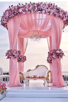 an outdoor wedding setup with pink drapes, flowers and chandelier on the beach