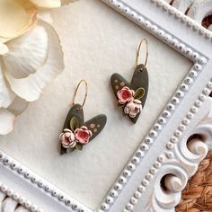 two earrings with flowers on them are sitting next to a flowery frame in front of a white flower