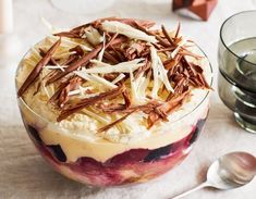 a dessert in a glass bowl with chocolate shavings on top and two glasses next to it