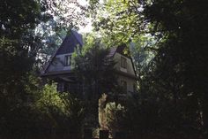 an old house is surrounded by trees and bushes on a sunny day in the woods