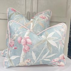 two blue and pink floral pillows sitting on top of a white bedding with an old door in the background