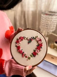 a woman holding a small embroidered heart with flowers