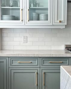 a kitchen with white cabinets and marble counter tops, gold pulls on the cupboards