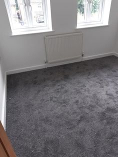 an empty room with two windows and no curtains on the wall, in front of a radiator