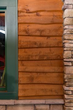 a cat sitting in the window of a wooden house with green shutters and wood siding