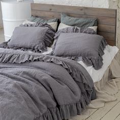 the bed is made with grey linens and ruffled pillows