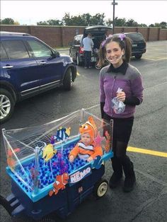 a woman standing next to a blue cart filled with nemo and clown fish toys