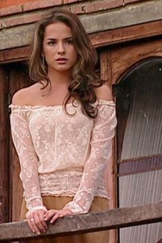 a woman standing on top of a balcony next to a wooden fence with her hands on her hips