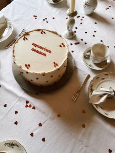 a white table topped with a cake covered in frosting next to two cups and saucers