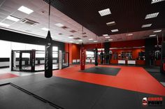 a gym with red walls and black flooring, punching bags in the middle of the room