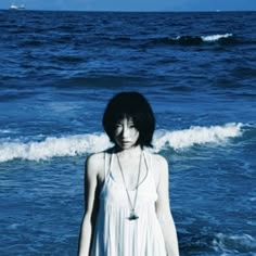 a woman standing in the ocean with her hands on her hips and wearing a white dress