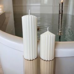 two white candles sitting on top of a bath tub